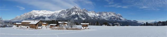 Eine winterliche Landschaft mit schneebedeckten Bergen und traditionellen Holzhäusern. Der Himmel ist klar und blau, ideal für Winteraktivitäten.