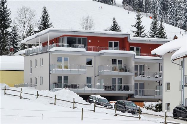 A modern building in the snow, surrounded by a wintry landscape. In the background, there are snow-covered trees and a slope visible.
