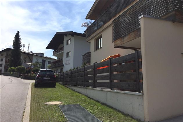 Modernes Haus mit einem parkenden Auto davor. Die Umgebung ist grün mit einem klaren blauen Himmel.