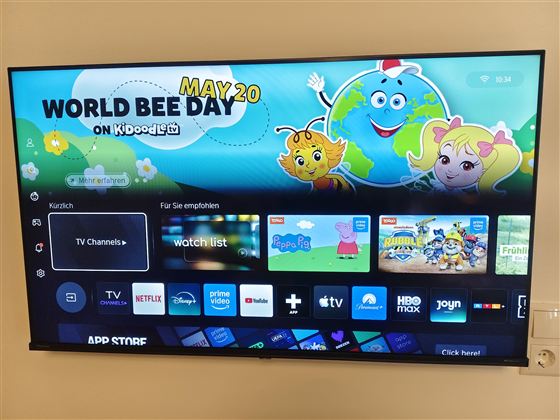 Een televisie toont een kleurrijke gebruikersinterface met het thema "Wereldbijendag". Verschillende apps en aanbevelingen voor kinderinhoud zijn zichtbaar.