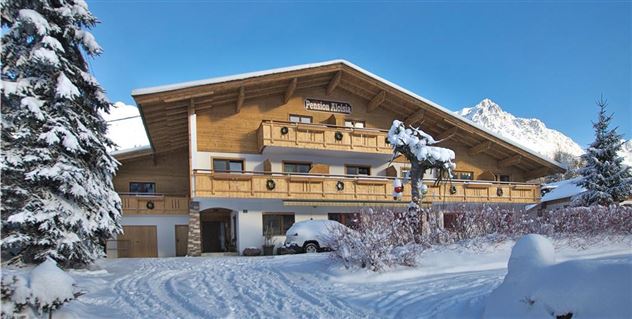 Ein charmantes Holzhaus im Winter mit schneebedeckter Umgebung. Kristallklarer Himmel und verschneite Bäume umgeben die Unterkunft.