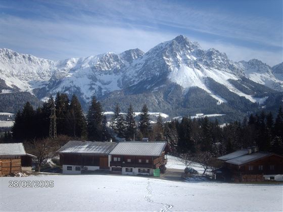 A snowy landscape with high mountains in the background. In the foreground, traditional wooden houses stand.