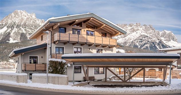 Ein modernes Haus im alpinen Stil, umgeben von Schnee und Bergen. Die Fassade aus Holz und der Balkon verleihen dem Gebäude einen einladenden Charakter.