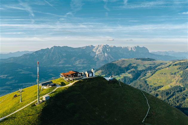 Een schilderachtig berglandschap met een hut en een kleine kerk. Op de achtergrond rijzen majestueuze bergen op onder een heldere lucht.