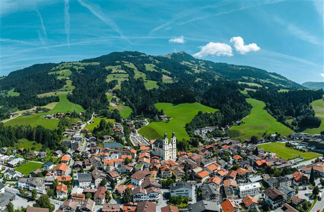 Een schilderachtig dorp omgeven door groene heuvels en bergen. De architectuur is traditioneel met veel rode daken en een opvallende kerk.