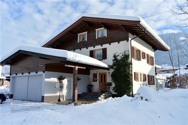 A beautiful two-story house with a gabled roof, surrounded by snow. The sky is clear with some clouds.