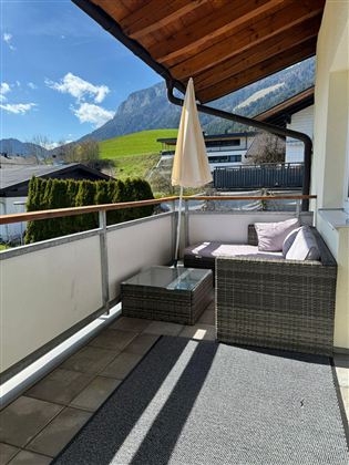 A balcony with a cozy lounge area and a sunshade. In the background, green meadows and mountains can be seen.