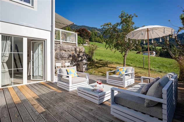 Einzigartige große Holz-Terrasse mit unverbautem Ausblick in die umliegende Berglandschaft. Moderne Terrassenmöbel, die zum Entspannen einladen und den ganzen Tag Sonne bieten. Ein moderner Gasgriller der Marke Napoleon steht für entspannte Grillabende bereit.