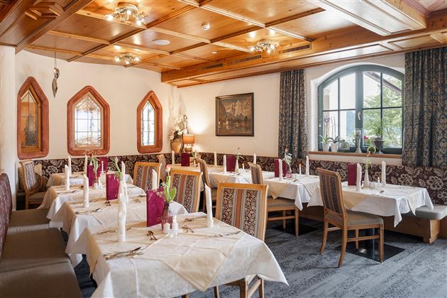 Ein gemütliches Restaurant mit elegant eingedeckten Tischen und Holzdecke. Große Fenster sorgen für angenehmes Licht und eine einladende Atmosphäre.