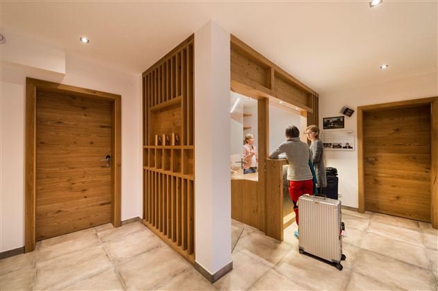 Ein moderner Empfangsbereich mit hellem Innenraum und Holzverkleidungen. Zwei Personen stehen an einem Empfangstresen, während Gepäck in der Nähe steht.