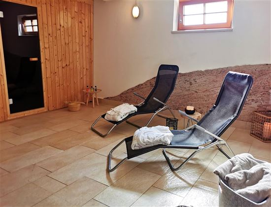 Ein entspannender Wellnessbereich mit zwei Liegen und einem warmen, einladenden Ambiente. Die Wände sind aus Holz, und es gibt sanfte Beleuchtung sowie dekorative Elemente.