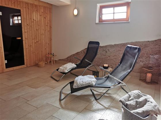 Ein entspannender Wellnessbereich mit Liegen und sanfter Beleuchtung. Die Holzverkleidung und der Türbereich schaffen eine gemütliche Atmosphäre.
