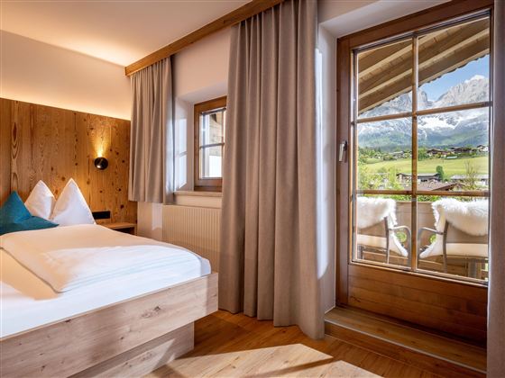 Een gezellige kamer met houtafwerking en een groot raam. Door het raam ziet men het schilderachtige berglandschap.