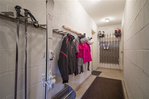 Ein Flur mit Skiausrüstung und Winterkleidung an der Wand. Aufhänger für Skier und Schneeausrüstung sind sichtbar.