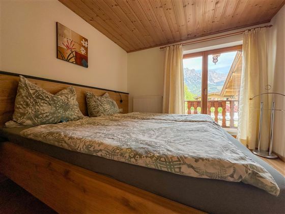 Een gezellig slaapkamer met een tweepersoonsbed en twee kussens. De grote ramen bieden uitzicht op de bergen en veel daglicht.