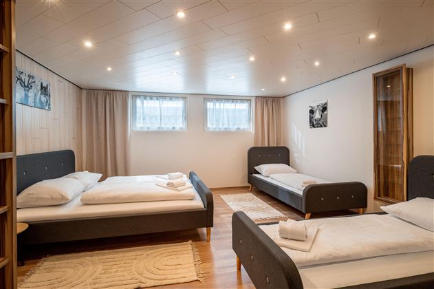 Ein einfaches Schlafzimmer mit zwei Betten und einem gemütlichen Holzfußboden. Die Wände sind hell und das Zimmer hat großes, natürliches Licht.