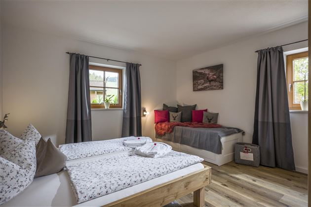 Ein gemütliches Schlafzimmer mit zwei Einzelbetten und einem Tagesbett. Große Fenster sorgen für viel Tageslicht und eine angenehme Atmosphäre.