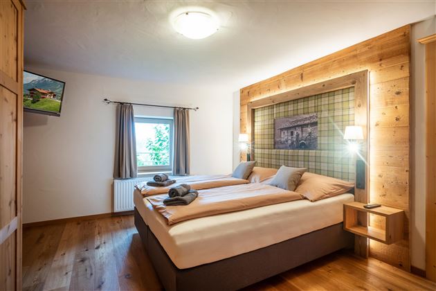 A cozy bedroom with two beds and warm wooden furniture. Large windows provide plenty of daylight.