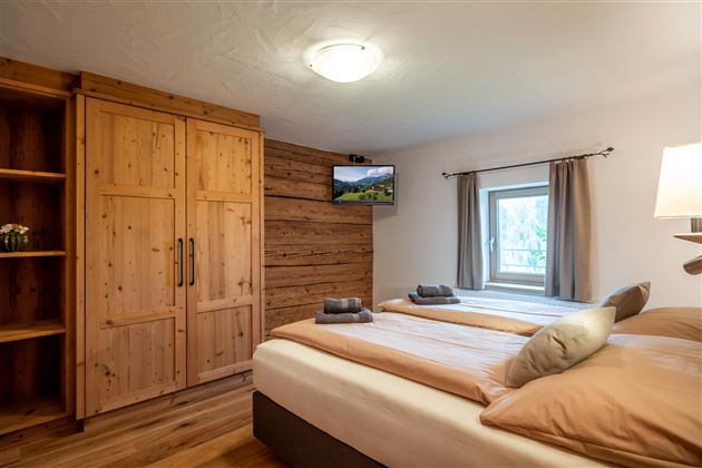 A cozy bedroom with two beds and wooden-paneled walls. There is a television and a window sill with a view from the window.