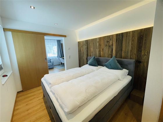 A modern bedroom with a double bed and wood paneling. The room is designed to be bright and cheerful.