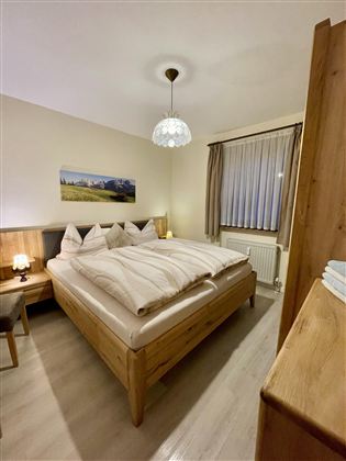 Een gezellig slaapkamer met een groot bed en houten meubels. Zachte verlichting en een raam zorgen voor een uitnodigende sfeer.