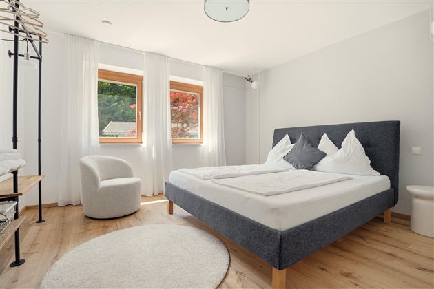 Ein modernes Schlafzimmer mit einem großen Bett und hellen Fenstern. Der Raum ist stilvoll und gemütlich eingerichtet.