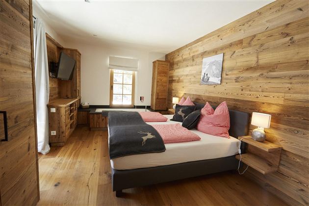 Ein gemütliches Schlafzimmer mit Holzwänden und zwei Betten. Die dekorativen Kissen in Rosa und Schwarz verleihen dem Raum eine einladende Atmosphäre.