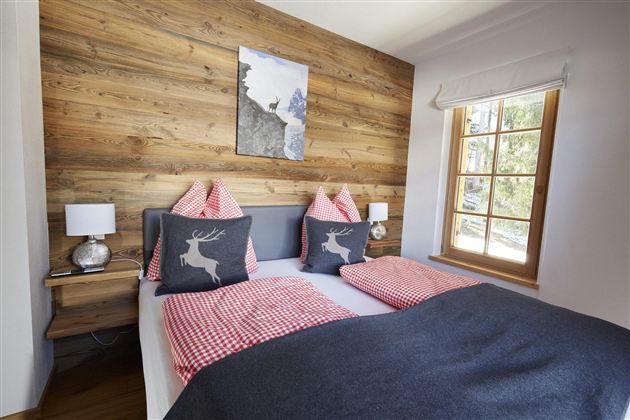 Ein gemütliches Schlafzimmer mit einem Holzpanel-Wand und einem großen Fenster. Das Bett ist mit karierten Kissen und einer Decke dekoriert.