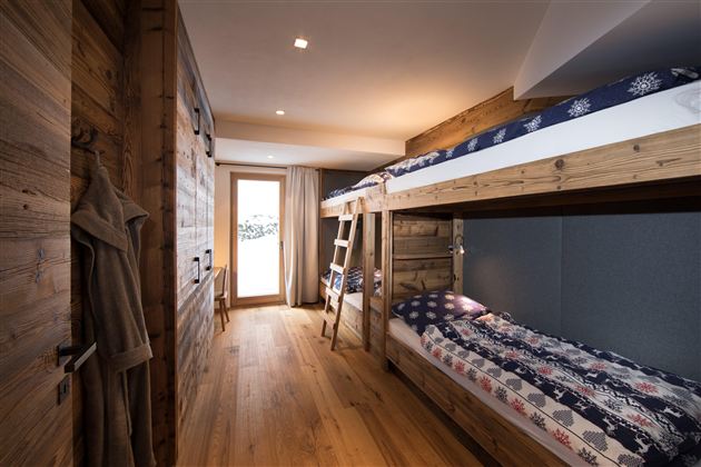 Ein gemütliches Zimmer mit einem Etagenbett und Holzverkleidung. Große Fenster bieten einen Blick ins Freie und viel Tageslicht.