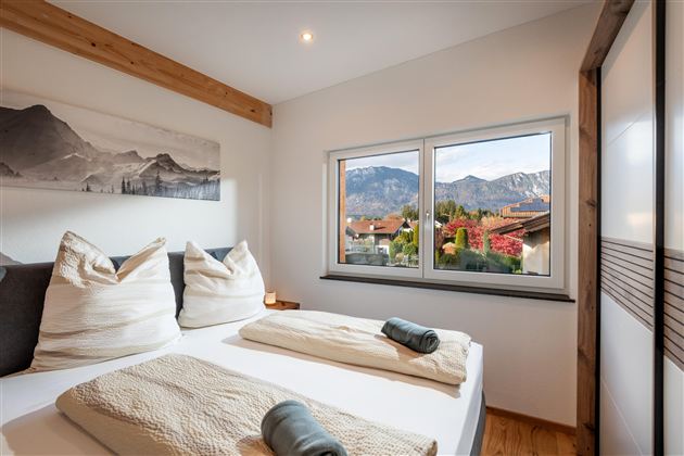 Ein modernes Schlafzimmer mit zwei Betten und großen Fenstern. Draußen ist eine schöne Berglandschaft zu sehen.