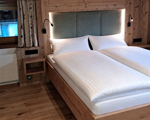Ein gemütliches Schlafzimmer mit einem Doppelbett und hellem Holzinterieur. Die Wände sind mit dezenten Vorhängen und modernen Lampen dekoriert.