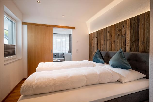 Ein modernes Schlafzimmer mit zwei Einzelbetten und stilvollen Kissen. Die Wände sind teilweise mit Holz verkleidet, und viel Tageslicht strömt durch das Fenster.
