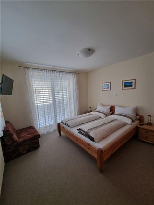 Een heldere slaapkamer met twee eenpersoonsbedden en een gezellige stoel. Grote ramen met lichtgordijnen zorgen voor een aangename sfeer.