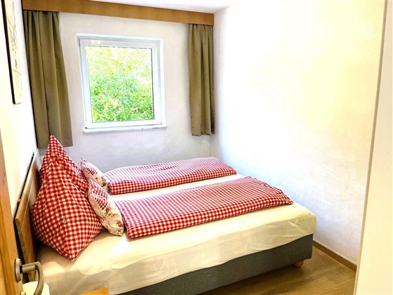 Ein gemütliches Schlafzimmer mit zwei Einzelbetten und karierten Kissen. Das Fenster bietet Blick auf die grüne Umgebung.