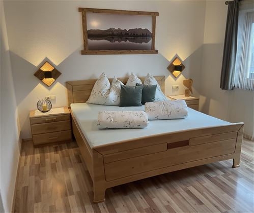 Ein modernes Schlafzimmer mit einem großen Holzbett und Kissen. Sanfte Beleuchtung schafft eine gemütliche Atmosphäre.