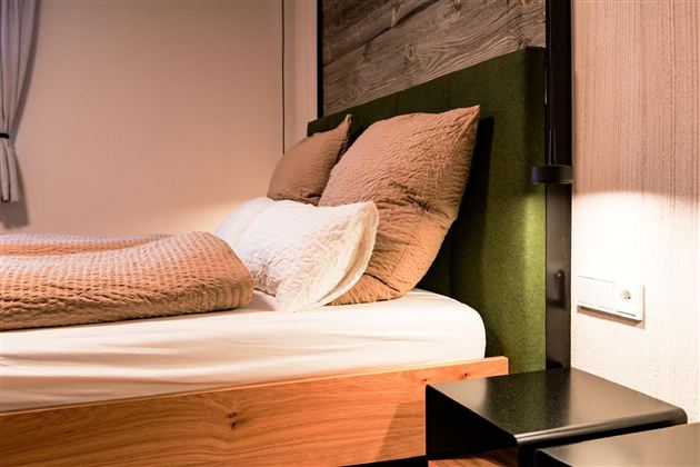 A modern bedroom with a cozy bed and two pillows. Next to the bed is a black nightstand.