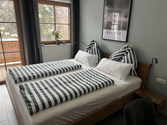 Een gezellige slaapkamer met een twijfelaar en gestreepte dekbedden. Grote ramen zorgen voor veel daglicht en een uitzicht naar buiten.