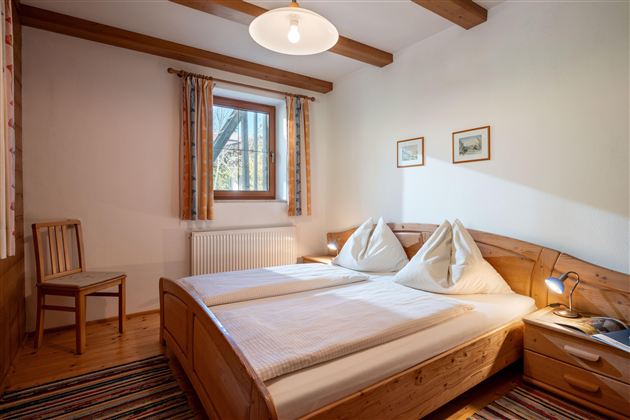 Ein gemütliches Schlafzimmer mit zwei Betten und farbenfrohen Bettwäsche. Ein Fenster mit Pflanzen und sanftem Licht sorgt für eine einladende Atmosphäre.