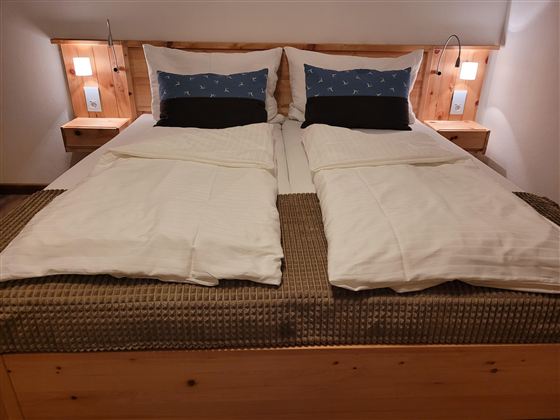 A cozy bedroom with a large bed and two pillows. The walls are light and there are night lights on the sides.