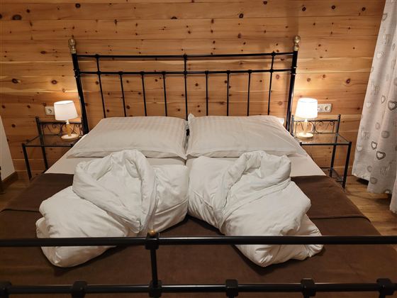 A cozy bedroom with a metal bed and two pillows. The wooden walls and soft lights create an inviting atmosphere.