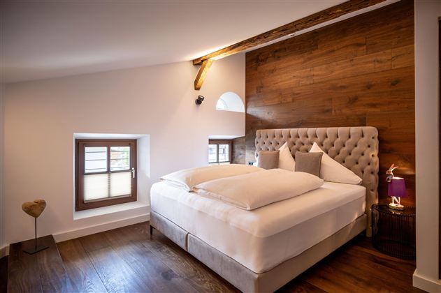 A cozy bedroom with a large, comfortable bed and wood decor on the wall. The room has large windows that provide plenty of daylight.