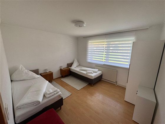 A simple room with two single beds and minimalist decor. There is a bright wooden floor and plenty of natural light coming through the window.