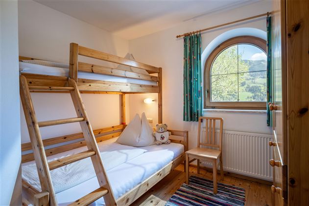 Ein gemütliches Zimmer mit einem Etagenbett und einem einzelnen Stuhl. Große Fenster bieten einen Blick auf die Natur draußen.