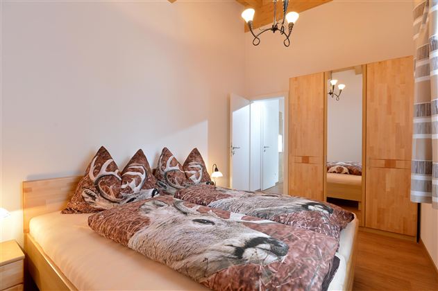 Ein gemütliches Schlafzimmer mit einem Doppelbett und Fellen mit Tiermotiven. Es gibt einen Kleiderschrank und einen großen Spiegel, die für genügend Stauraum sorgen.