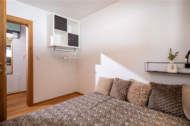 A cozy room with a bed and decorative cushions. On the wall, there is a shelf with a plant and another storage space.