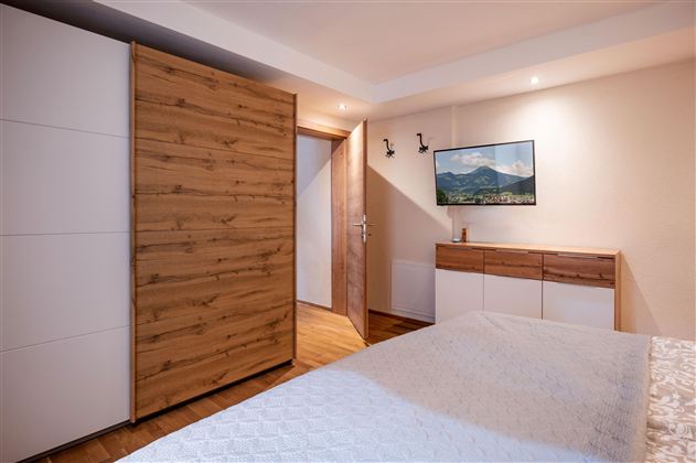 Ein modernes Schlafzimmer mit einem großen Bett und einem Holzschrank. An der Wand hängt ein Bild von einer Landschaft.