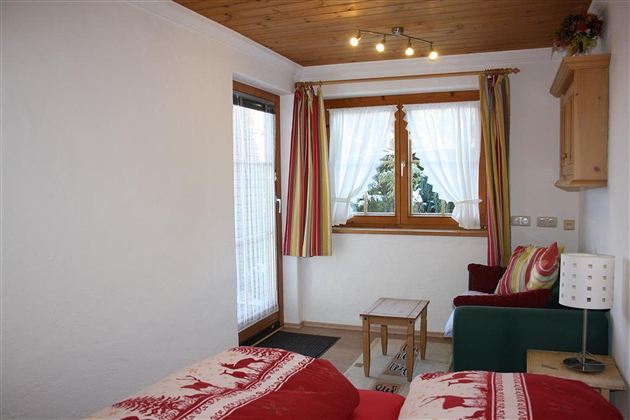 Ein gemütliches Zimmer mit einem Fenster, das viel Licht hereinlässt. Farbig gestreifte Vorhänge und eine kleine Sitzecke sorgen für eine einladende Atmosphäre.