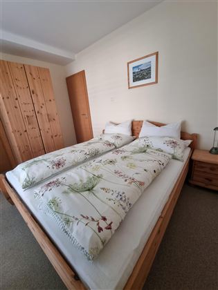 Een gezellige slaapkamer met een tweepersoonsbed en frisse dekbedden. De kamer heeft een houten kast en een schilderij aan de muur.