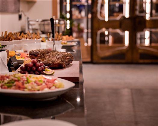 A refined buffet with various dishes, including meat, meat dishes, and fresh vegetables.  
The table is elegantly set and offers an inviting atmosphere.