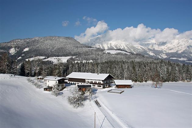 Eine winterliche Landschaft mit schneebedeckten Feldern und Bergen. Ein gemütliches Haus steht in der Mitte der Szene.